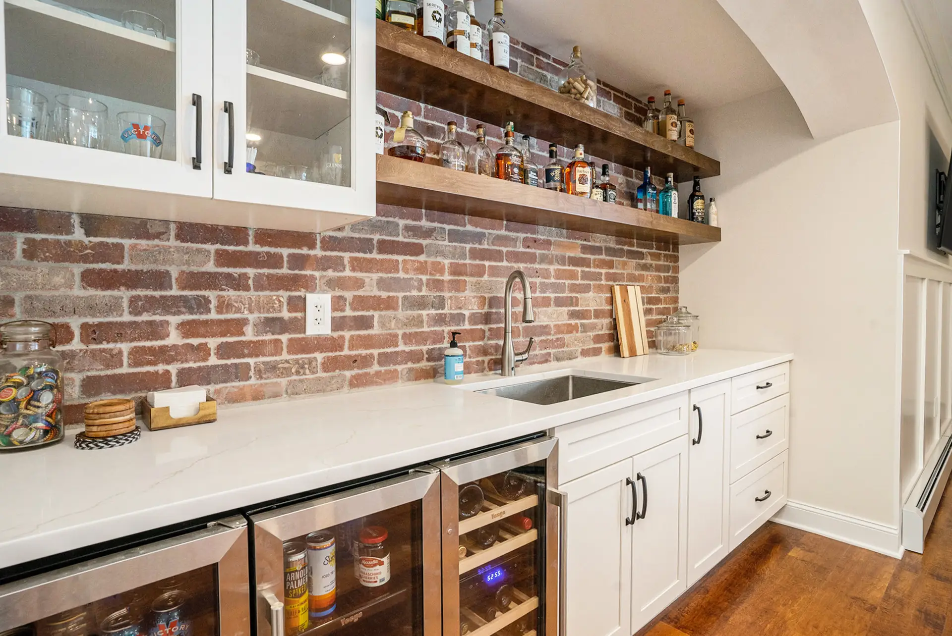 Home bar with exposed brick backsplash, floating wood shelves, and beverage centers