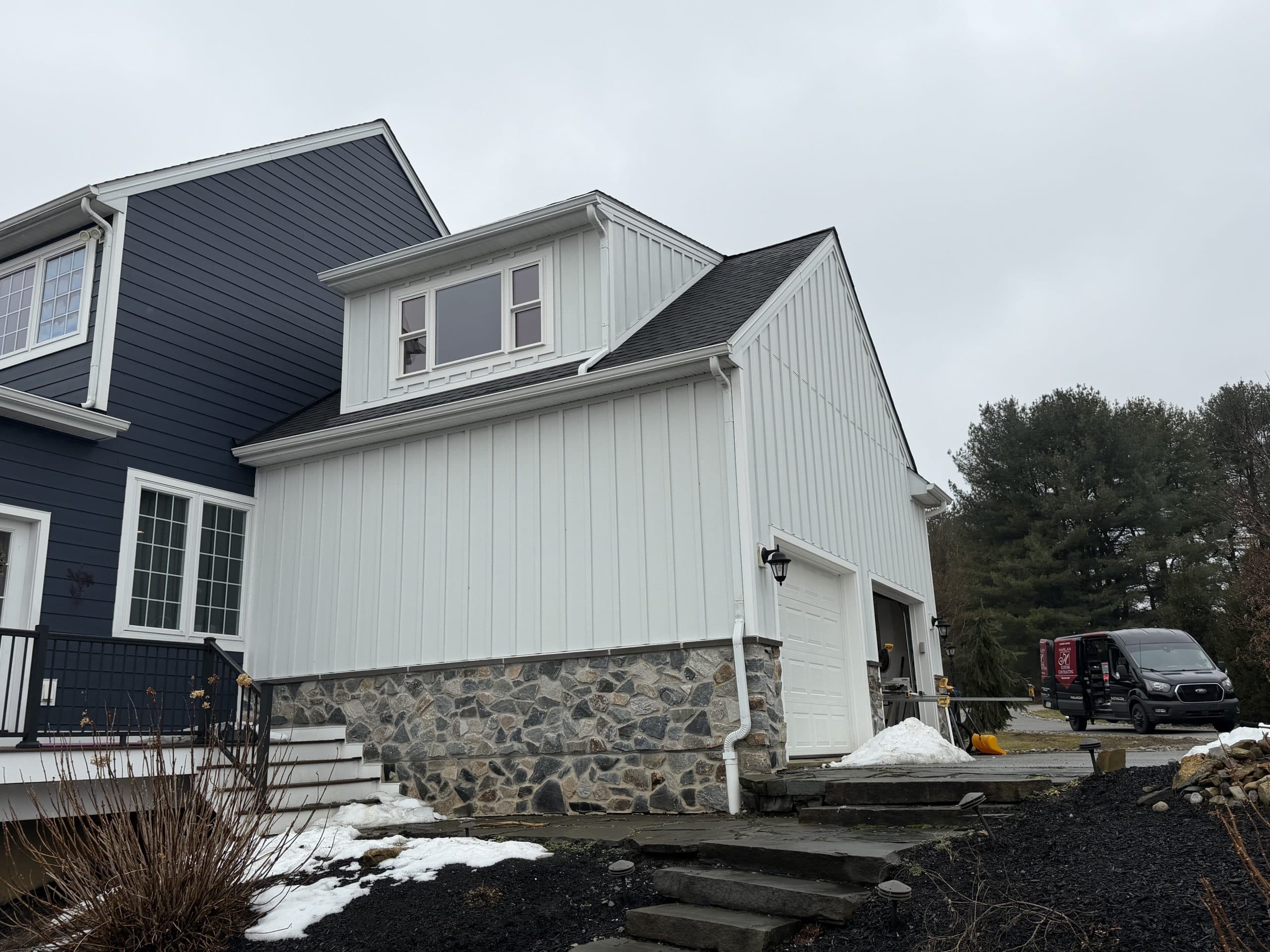 Two-story addition with new white board-and-batten siding and stone veneer base by Harlan Custom Contracting